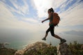 Hiker jumping on seaside mountain peak rock