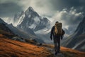 A hiker with a large backpack on a mountain path with dramatic peaks in the background and autumn-colored grass in the