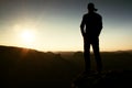 Hiker in long cap on rock empire and watching to Sun. Beautiful moment the miracle of nature