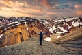 Hiker man standing with arms raised on the cliff with volcanic mountain and snow covered from Blanhjukur trail on summer in the