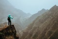 Hiker with map in steep rocky terrain in front of a incredible panorama view of high mountain ranges deep ravines and