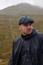 Hiker with a poncho and baret in the Scottish Highlands. raining.