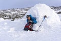 Hiker pours himself a tea from a thermos, sitting in a snowy house igloo