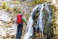 Hiker with a red backpack observes a waterfall