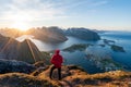 Hiker in red jacket are standing on top of the famous Reinebringen overlooking Reine and Hamnoy in the Lofoten islands during the