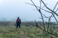 A hiker with red ruck sack standing in the distance in a out of focus. On a foggy, winters day in the countryside