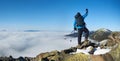 Hiker on rocky hill on background of valley with white clouds, snowy mountains and blue sky. Royalty Free Stock Photo