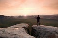 Hiker on sharp cliff in rocky empires park, watching over misty and foggy morning gulch to horizon.