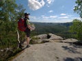 Hiker in shorts wear cowboy hat and red back pack, stay on rock