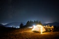 Hiker sitting near illuminated camp tent under night starry sky. Royalty Free Stock Photo