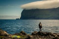 Hiker standing at the rocky shore near Mikladalur village looking at the Kunoy island, Kalsoy island, Faroe Islands