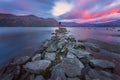 Hiker staring at the pink beauty of clouds movements over a stones jetty at dawn at Lake Wanaka in New Zealand