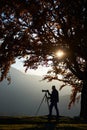 Hiker tourist man with camera on grassy valley on background of mountain landscape under big tree. Royalty Free Stock Photo