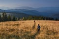 Hiker is walking along the trail through tall grass in the mountains. View on the wooded hills and hazy peaks in the distance. Royalty Free Stock Photo