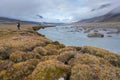 Hiker walking by Owl river in remote arctic valley on a partly cloudy summer day. Dramatic arctic landscape of Akshayuk