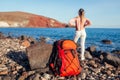 Hiker woman with backpack walking on Red beach on Santorini island, Greece enjoying sea landscape. Royalty Free Stock Photo