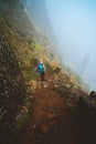 Hiker women with backpack walking down the trekking path. The steep arid slope of the rock. The fog encase the mountain