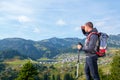 Hiker young man with backpack and trekking poles standing on edge of cliff and looking at the lake, rear view