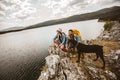 Hikers with backpacks and their doberman sitting on cliff enjoying at the mountain lake