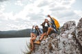 Hikers with backpacks and their doberman sitting on cliff enjoying at the mountain lake