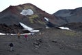 Hikers on black lava in front of a colorful hill and snow in Kamchatka, Russia