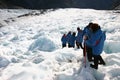 Hikers in single file descending rugged icy slope at glacier exploration