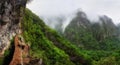 Hikers walking on a narrow path on the edge of the rock during Levada do Caldeirao Verde Trail. Misty green mountains in