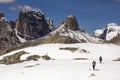 Hikers walking through a snowy landscape and surrounded by large mountains of dolomitic rock in the dolomite alps