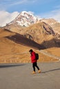 hiking alone in mountainous region. Backpacker walking down hillside road with snowy mountain and blue sky on background Royalty Free Stock Photo