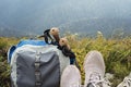 Hiking backpack, trekking poles and legs in sports shoes of young woman resting in mountain hike in valley, active healthy