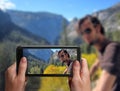 Young male hiker relaxing on top of a mountain.Hand is taking a photograph with a smartphone of the man together w