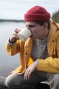 Hipster traveler in yellow raincoat holding metal mug. 