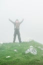 Hiking man with backpack open arms on foggy mountain peak Royalty Free Stock Photo