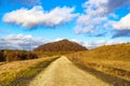 Hiking path between plain and hills with a mountain with autumn trees against blue sky Royalty Free Stock Photo