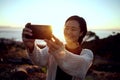 Hiking, selfie and Asian woman on mountain with sunset sky, smile and relax in nature on holiday adventure. Digital