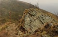 Hiking sign on a rock on a mountain slope next to a narrow rocky trail on a foggy day