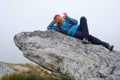 Hiking in Slovakia High Tatras mountains. Woman hiker rests on top of a large rock boulder, laying down, with fog around her