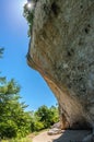 The hiking trail passes under the rock, the sun shines through the trees