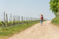 Hiking Woman with brown hair, straw hat and backpack hiking next to a wine field, looking up in the sky, hiding her eyes from the