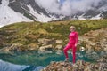 Hiking woman in red jacket stay at beautiful turquoise lake in mountains. Royalty Free Stock Photo