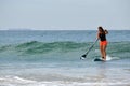 Unidentified surfer girl with an oar stands on a surfboard on the water in the Indian Ocean on a sunny day.