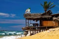 View on wooden bar restaurant with thatch roof on tropical beach with blue sky and rough sea waves Royalty Free Stock Photo