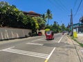 Hikkaduwa, Sri Lanka - March 13, 2022: The tourist hotel behind a high fence stands near the main road. Red tuk-tuk and people on