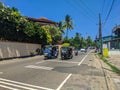 Hikkaduwa, Sri Lanka - March 13, 2022: The tourist hotel behind a high fence stands near the main road. Tuk-tuks, motorcycles and