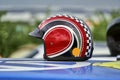 Classic driver helmet for racing with cars in black red design lies on a blue vehicle roof