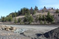 A hill with evergreen trees and bare deciduous trees next to train tracks and a gravel pit Royalty Free Stock Photo