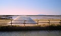 A hill of salt stands behind a canal and in front of salt pans and saltwater pools, at sunset near Marsala, Sicily