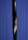 Hillary Clinton peaking out from behind blue curtains.