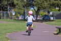 A little girl in a pink helmet, blue capri and striped long sleeve shirt riding red bike