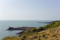 Hillside with dry and green grass against a blue ocean with a rocky shore in the sea Royalty Free Stock Photo